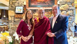 The Dalai Lama stands flanked by Carol and Sam Nappi in front of a stone fireplace