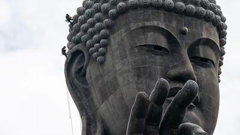 Close-up of the face of the statue with the two cleaners climbing it with ropes