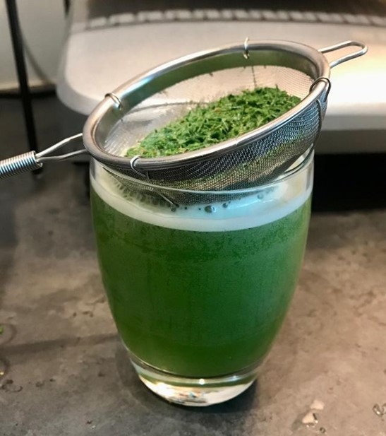 a strainer filled with pine needles above a glass of green liquid