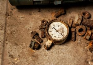 old corroded nuts and bolts are laying on a concrete floor with a rusty pressure valve in the middle