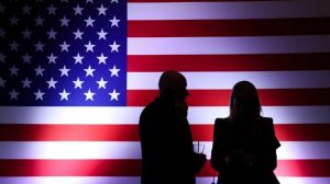 two figures silhouetted in front of an American flag