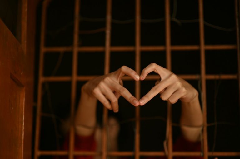 Hands through prison bars making heart shape