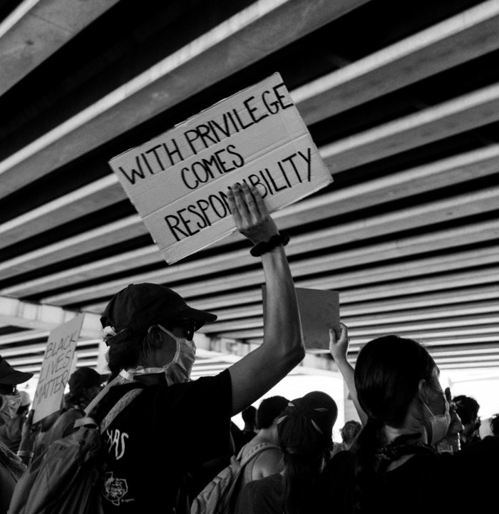 person in crowd holding poster that says with privilege comes responsibility (black and white)