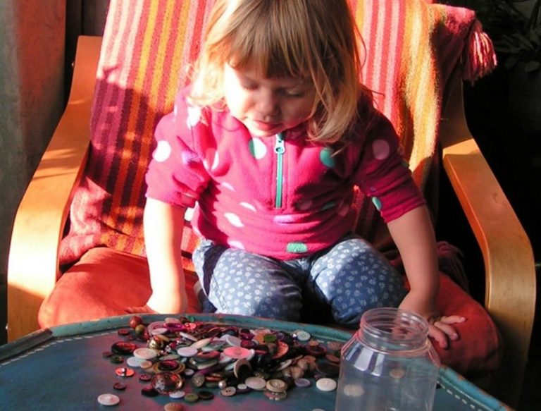 young girl in sunshine looking at a pile of buttons