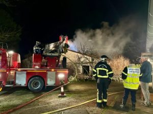 A fire truck and firefighters are seen with a burned building in the night